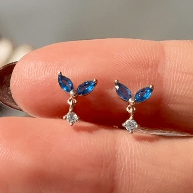 a person's hand holding a pair of blue and white earrings