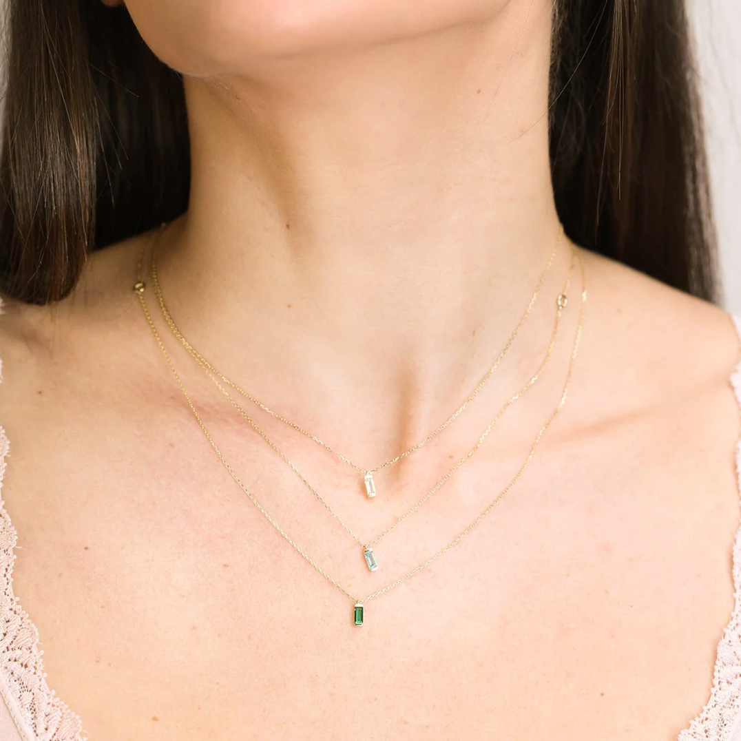 a woman wearing three layered necklaces including the emerald baguette necklace