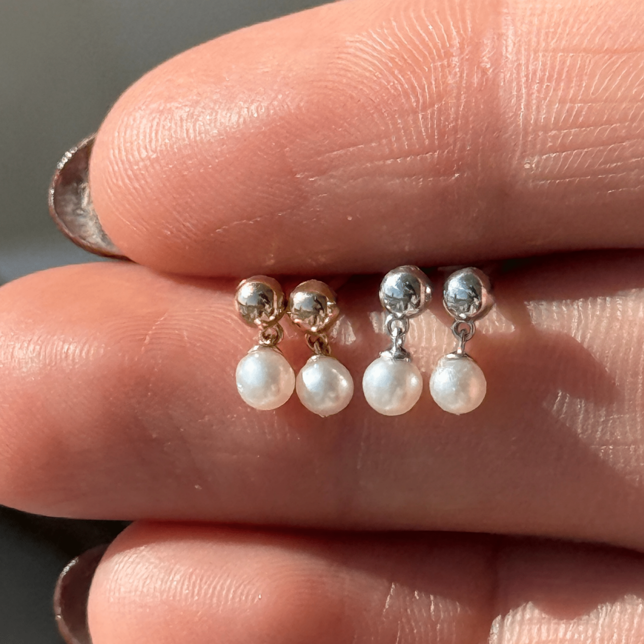 a person's hand holding three pearl and gold earrings