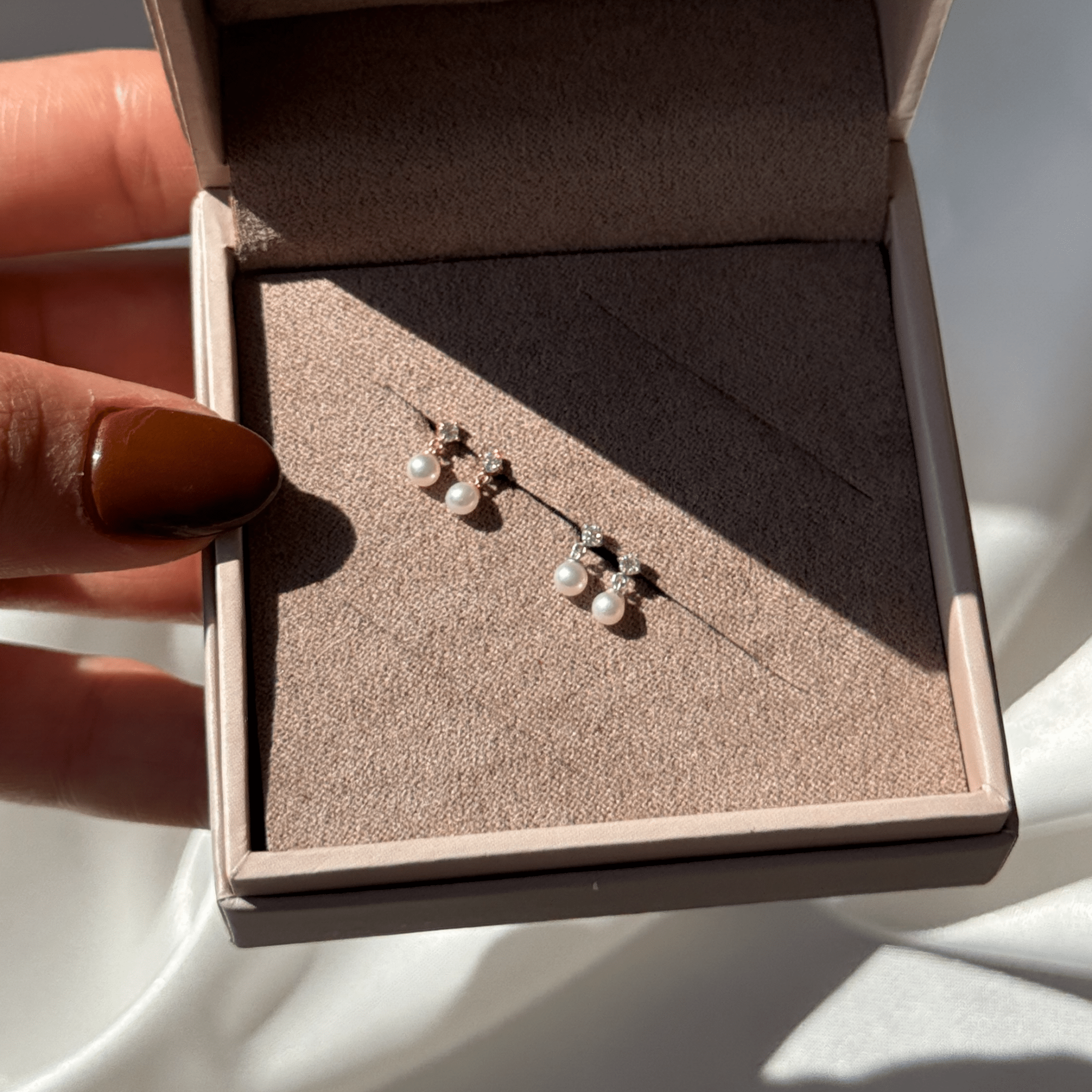 a woman's hand holding a pair of earrings in a box