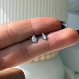 a person's hand holding a tiny ring with a tear shaped diamond on it