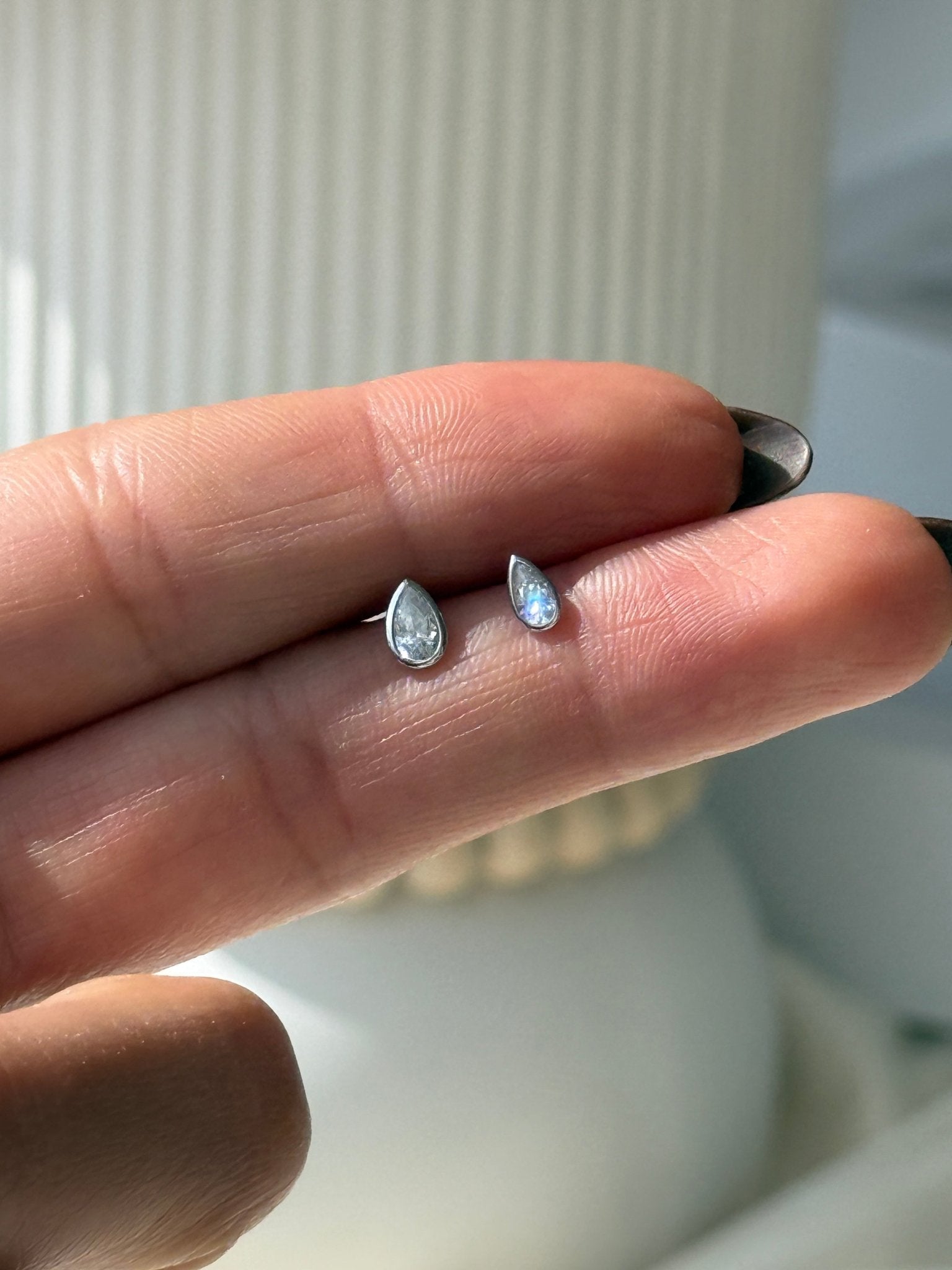 a person's hand holding a tiny ring with a tear shaped diamond on it