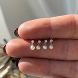 a person's hand holding a set of three pearl and diamond earrings