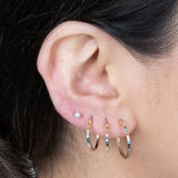 a model wearing three hoop earrings and a pearl stud