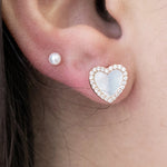 a model wearing a small pearl stud and a large heart stud