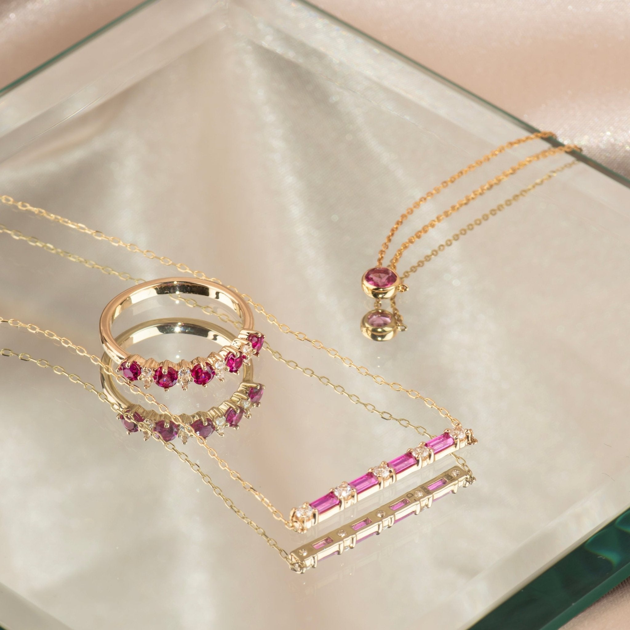 a pink gemstone ring and two necklaces on a mirrored surface.